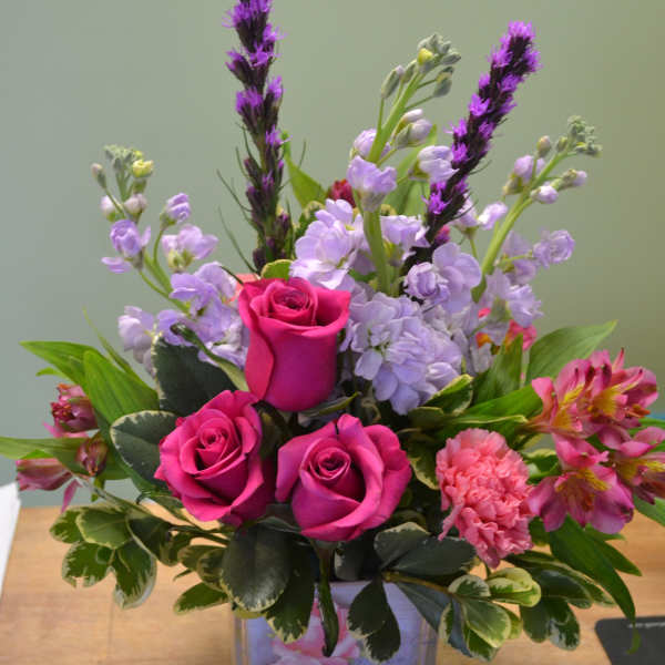 Pink roses and lavender flowers arranged in a clear square vase