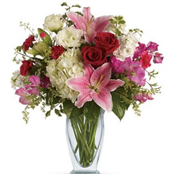 Bouquet of pink lilies, red roses, and white blooms in a glass vase
