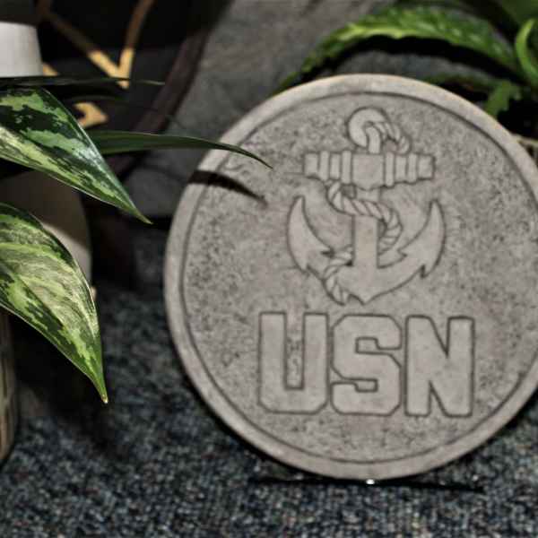 Round stone plaque with a USN anchor emblem surrounded by potted plants