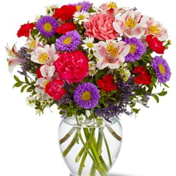 Mixed bouquet of pink, red, purple, and white flowers in a clear glass vase