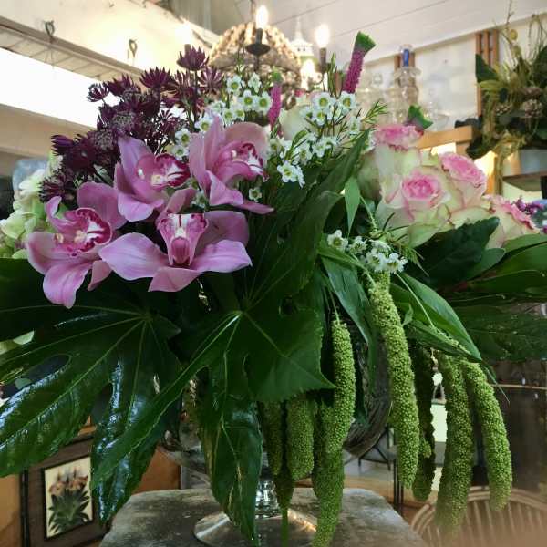 Pink orchids and roses arranged in a glass vase with large tropical leaves