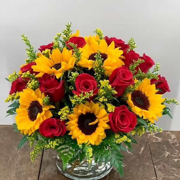 Bouquet of red roses and yellow sunflowers in a clear glass vase