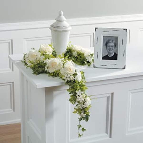 White rose floral tribute draped over a white urn