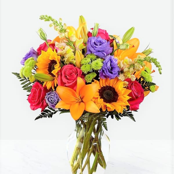 Bright mixed bouquet of roses, lilies, and sunflowers in a clear glass vase