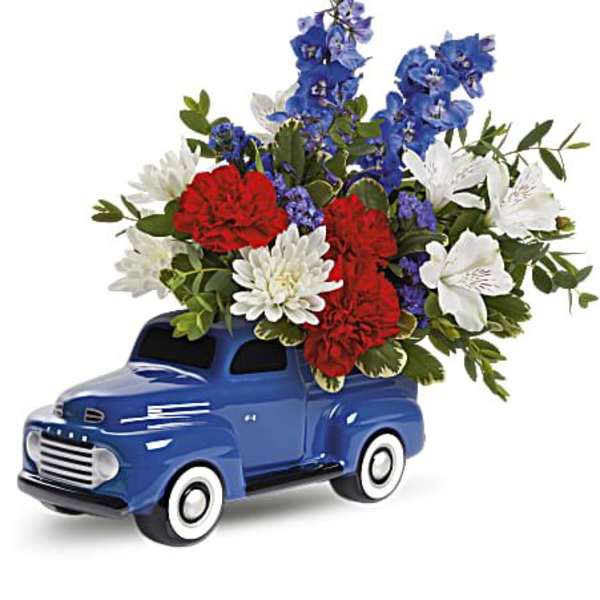 Blue vintage truck figurine holding a red, white, and blue flower arrangement