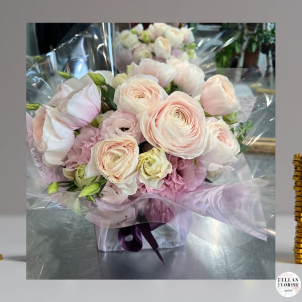 Hand-tied bouquet of pale pink and cream flowers in a clear box with cellophane wrap.