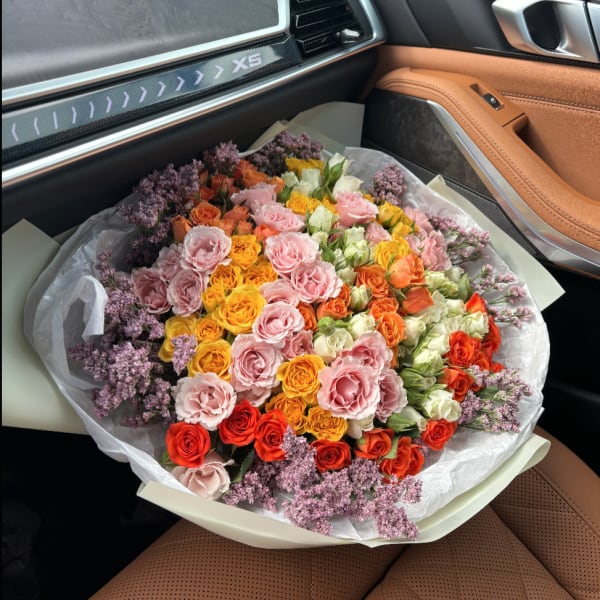 Large bouquet of pink, orange, yellow, and white roses with purple filler flowers