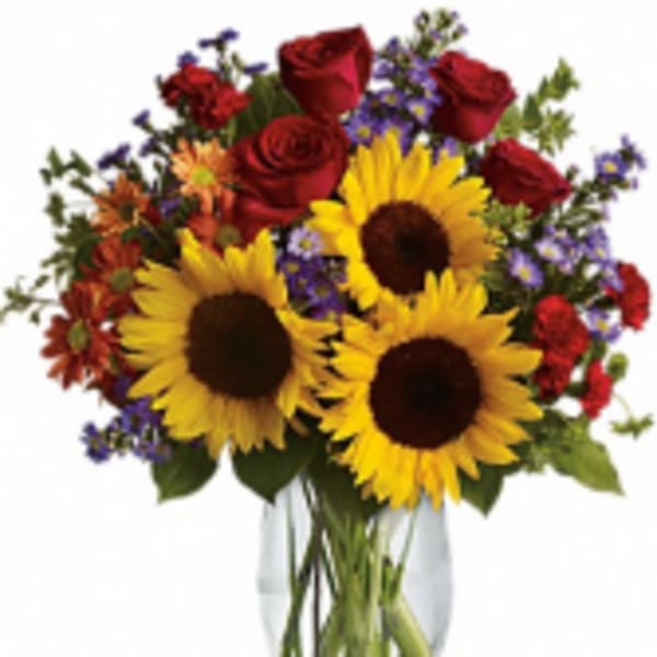 Bouquet of sunflowers, red roses, and purple flowers in a glass vase