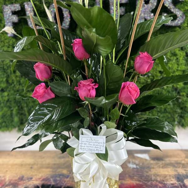 Pink roses arranged in a gold vase with a white ribbon bow