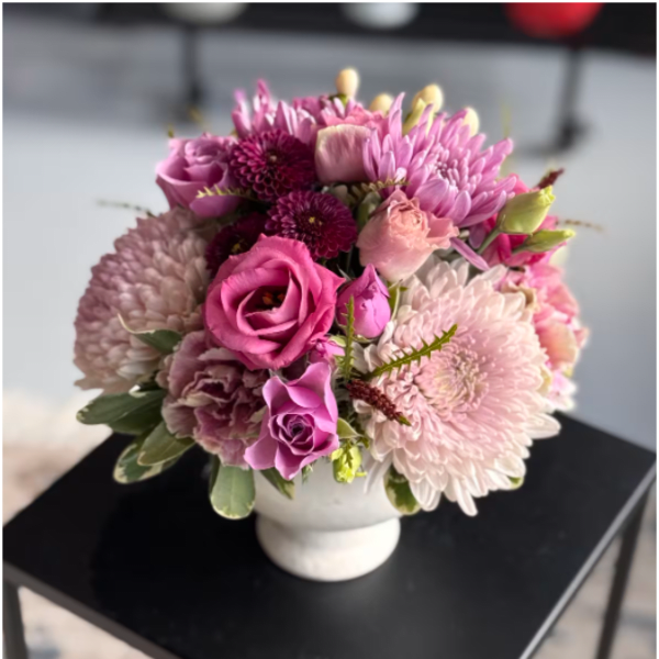 Compact arrangement of pink and purple roses and mums in a white ceramic vase