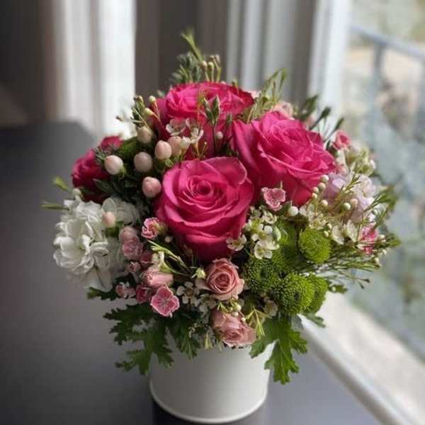 Pink rose bouquet in a white vase with small white and green accents