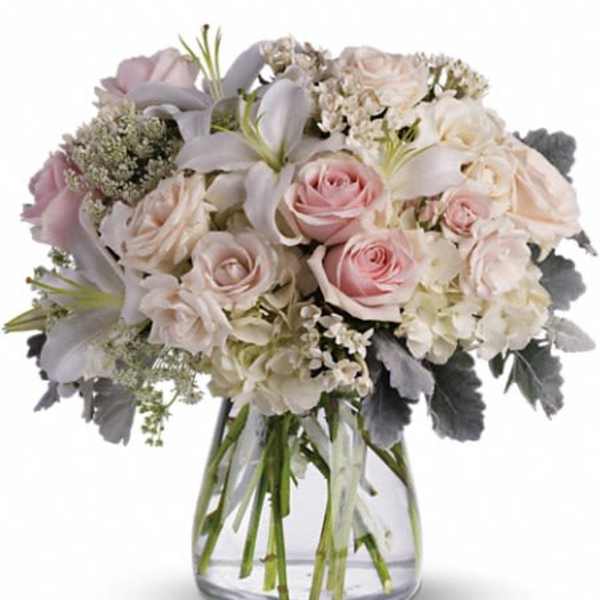 Arrangement of pale pink roses, white lilies, and hydrangeas in a clear glass vase