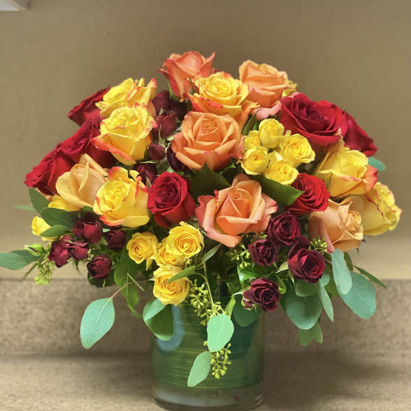 Mixed roses in red, yellow, and peach arranged in a glass vase