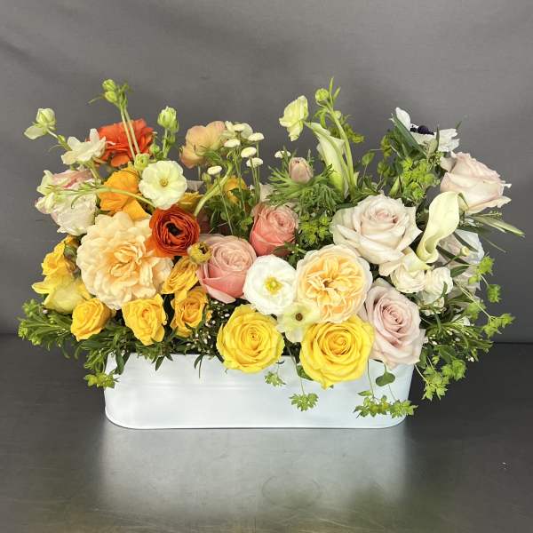 Mixed bouquet of roses and other blooms in a white rectangular container