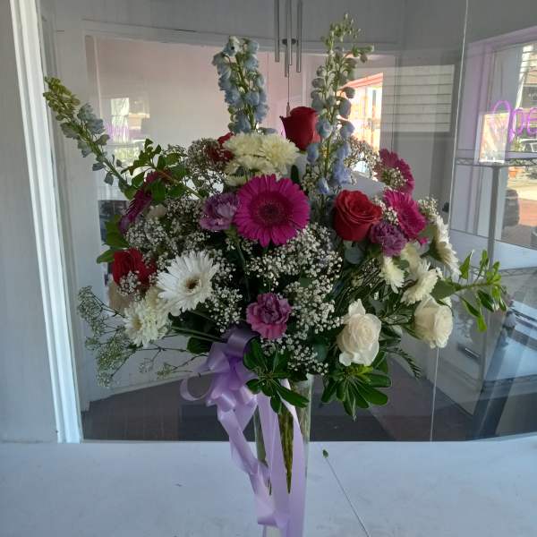 Tall mixed bouquet in a clear vase with purple ribbon