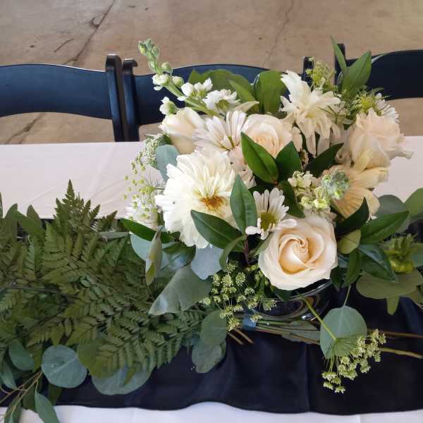 White floral arrangement with roses and daisies in a dark vase