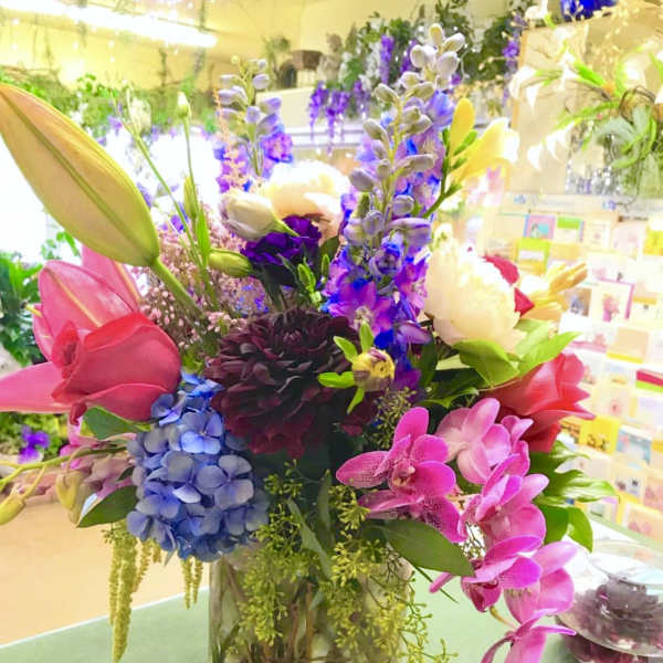 Colorful mixed bouquet in a clear glass vase with lilies, orchids, and hydrangeas