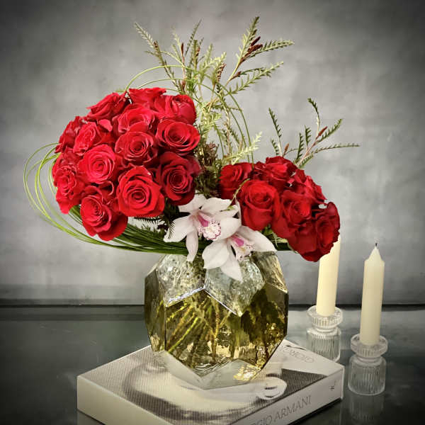 Red roses arranged in a gold geometric vase with white orchids