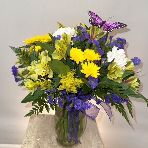 Bouquet of yellow and white flowers in a glass vase with a purple butterfly pick