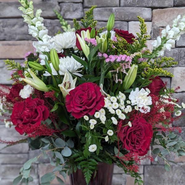 Bouquet of red roses, white lilies, and white snapdragons in a tall vase