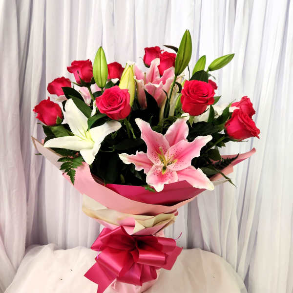 Bouquet of pink roses and lilies wrapped in pink paper with a ribbon