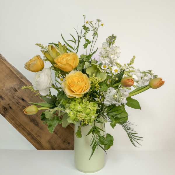 Tall arrangement of yellow roses, white flowers, green hydrangea and tulips in a pale vase
