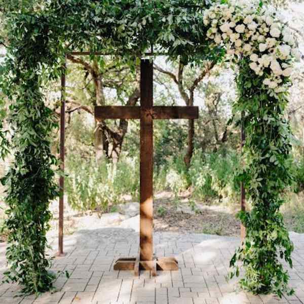 Wooden cross under a floral arch with white flowers and greenery