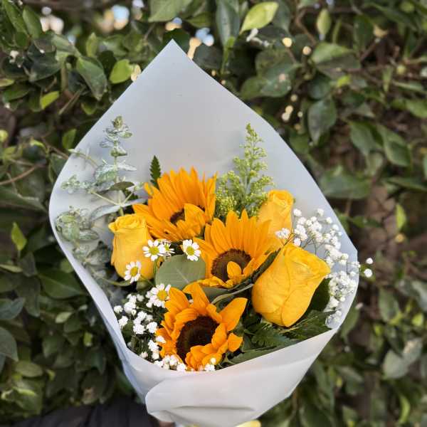 Hand-tied bouquet of bright yellow sunflowers and roses wrapped in white paper with a yellow ribbon