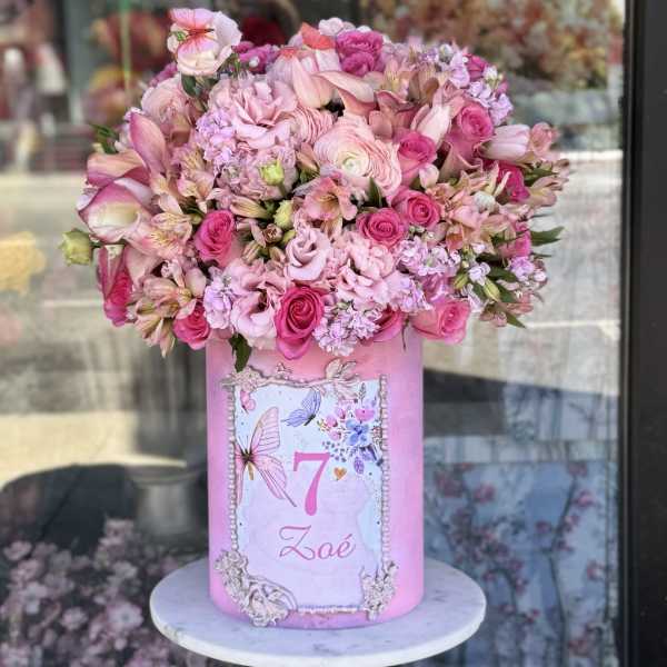 Pink floral arrangement in a decorated cylindrical box with a name label