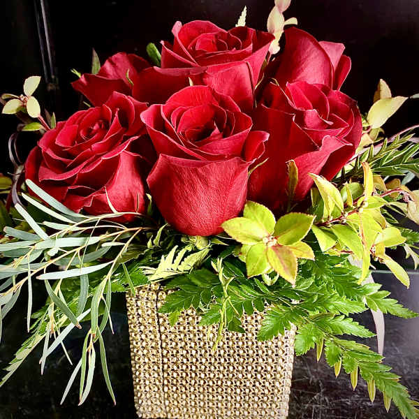 Low arrangement of red roses with foliage in a gold beaded cube vase