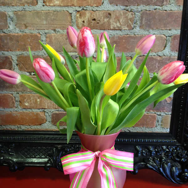 Pink and yellow tulips in a frosted pink vase tied with a striped pink and green ribbon bow.