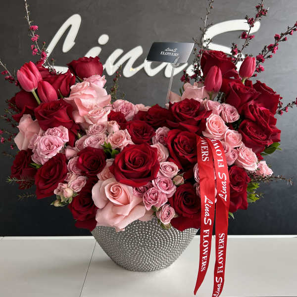 Large arrangement of red and pink roses in a silver vase with a red ribbon