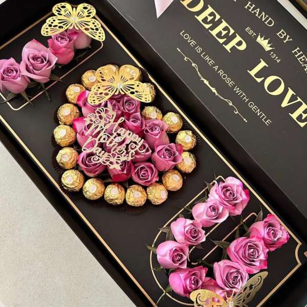 Black gift box with pink roses and chocolates arranged in compartments