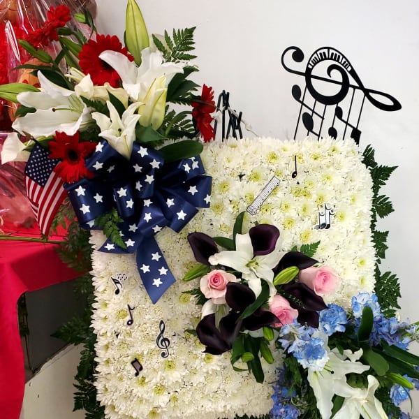 Floral standing spray with white lilies, red gerberas, and blue flowers on an easel