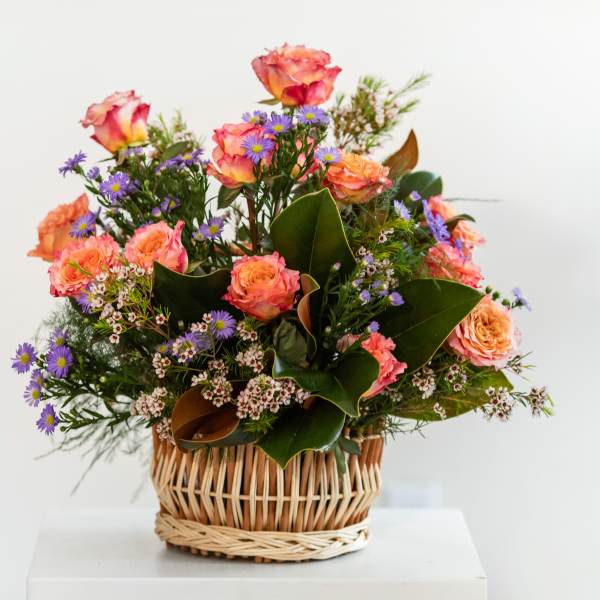 Basket arrangement of pink roses and purple daisies