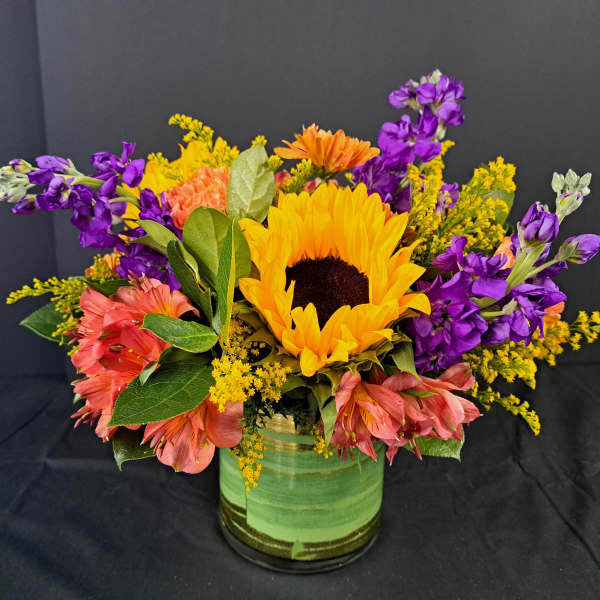 Sunflower bouquet with purple and pink flowers in a green glass vase