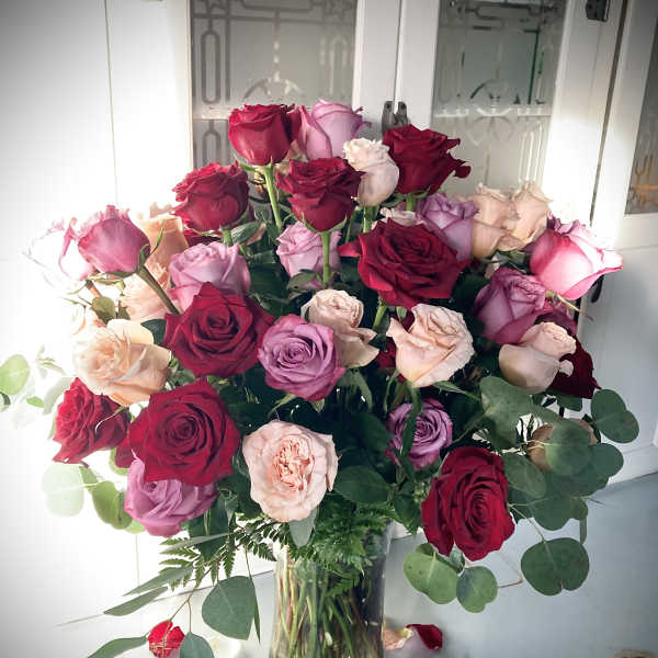 Bouquet of red, pink, and lavender roses in a clear glass vase