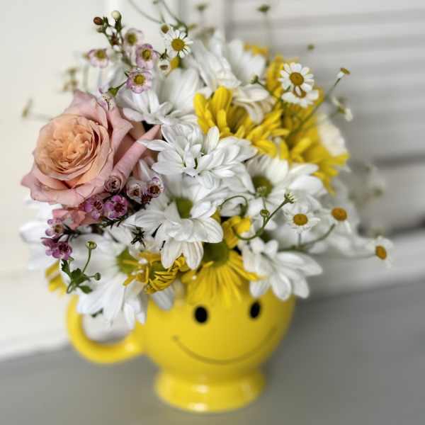 Bouquet of daisies and a peach rose in a yellow smiley-face mug