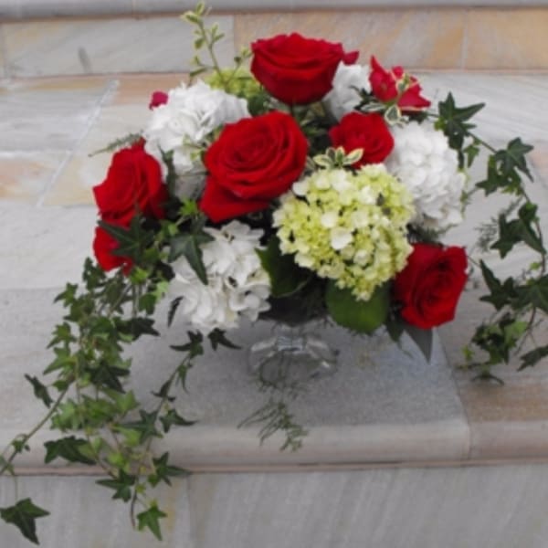 Red and white rose arrangement in a clear vase with trailing ivy