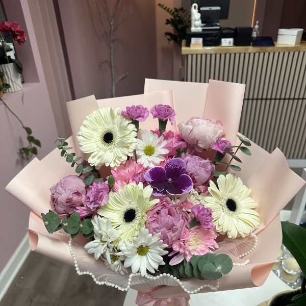 Pink bouquet with gerbera daisies, peonies, and orchids wrapped in blush paper