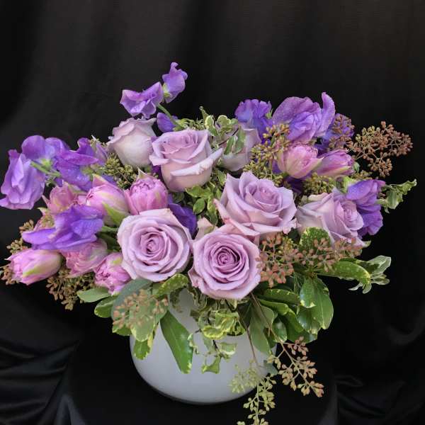 Lavender roses and purple sweet peas in a white vase