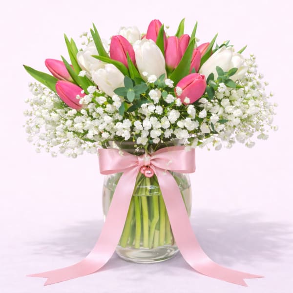 Pink and white tulips in a glass vase with a pink ribbon