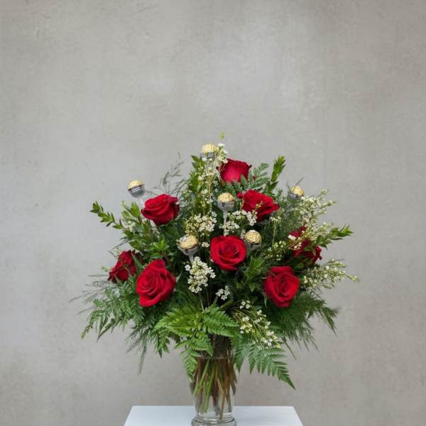 Red roses arranged in a clear glass vase with greenery and small white filler flowers