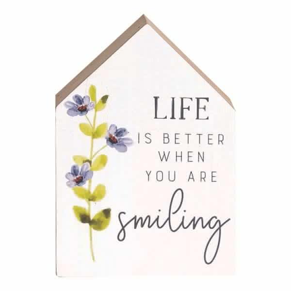 House-shaped wall sign with flowers and the words "Life is better when you are smiling"