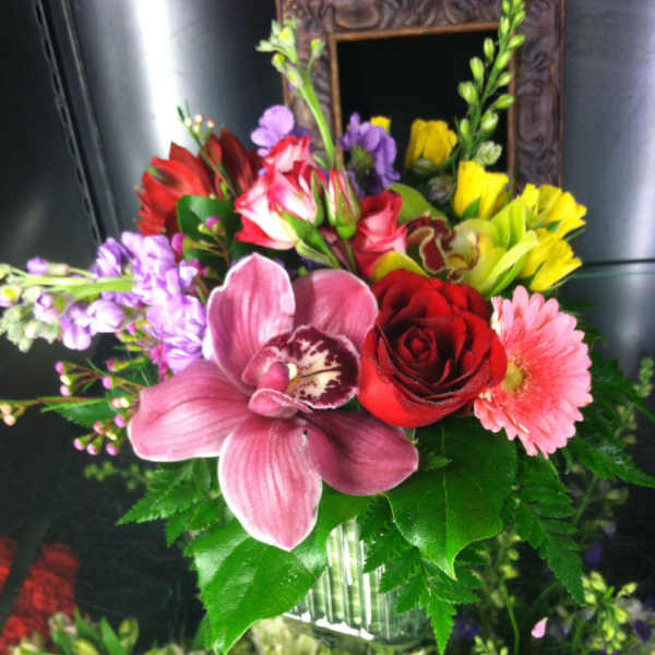 Mixed bouquet with pink orchid, red rose, pink gerbera and yellow blooms in a clear glass vase