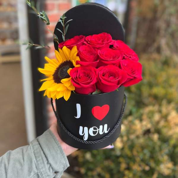 Red roses and a sunflower in a black heart-shaped box
