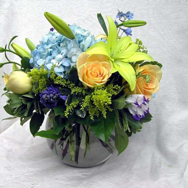 Mixed bouquet with blue hydrangea, yellow lilies, and peach roses in a glass vase