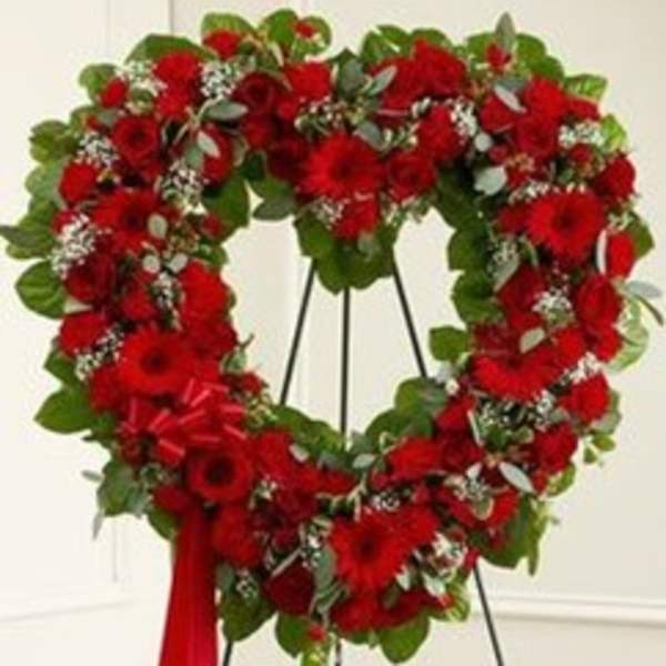 Heart-shaped red floral wreath on a stand with a red ribbon