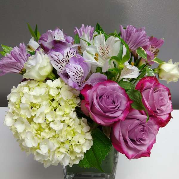 Bouquet of purple roses, white lilies, and pale hydrangea in a glass vase