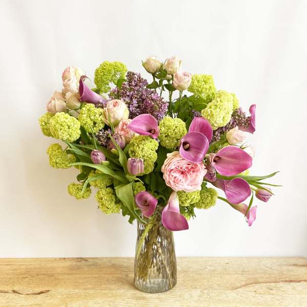 Bouquet of pink calla lilies, roses, and green hydrangeas in a glass vase